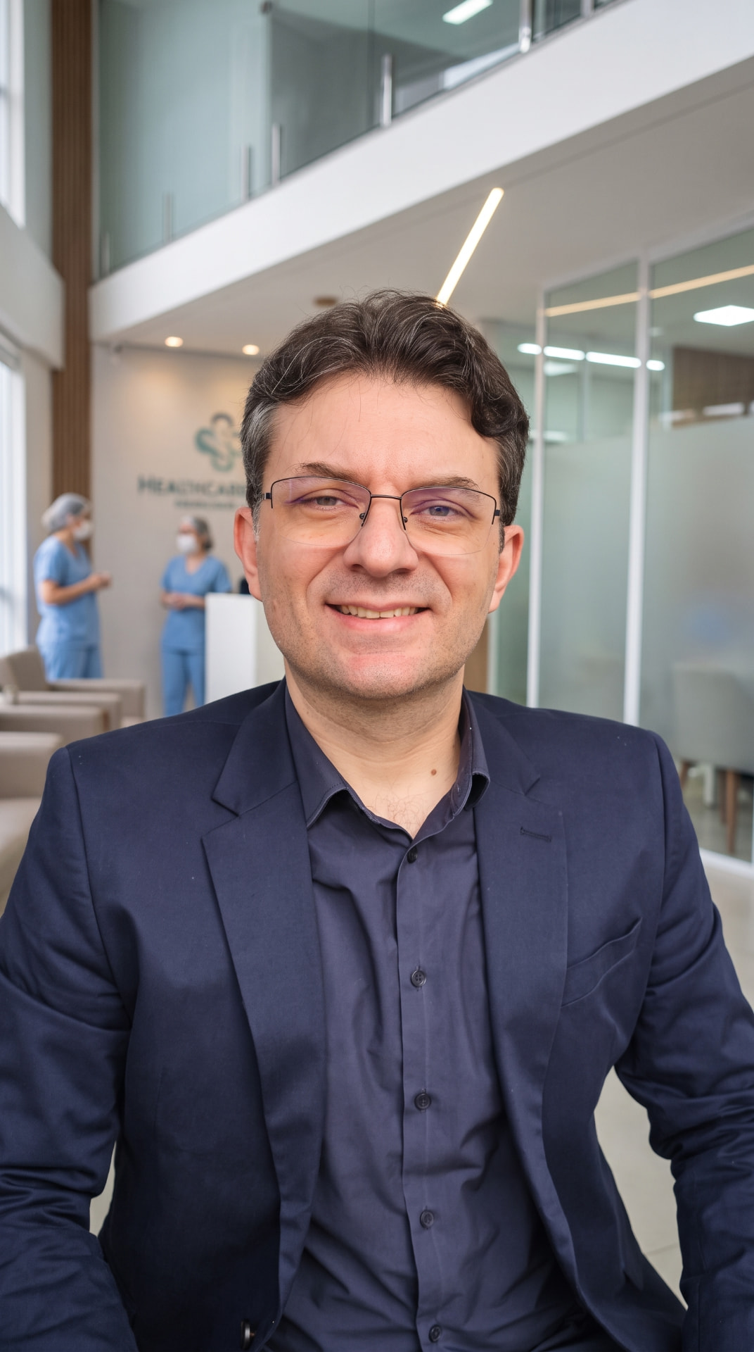 Dr. Flávio Delbem Chagas em seu consultório, vestindo blazer azul escuro e óculos.