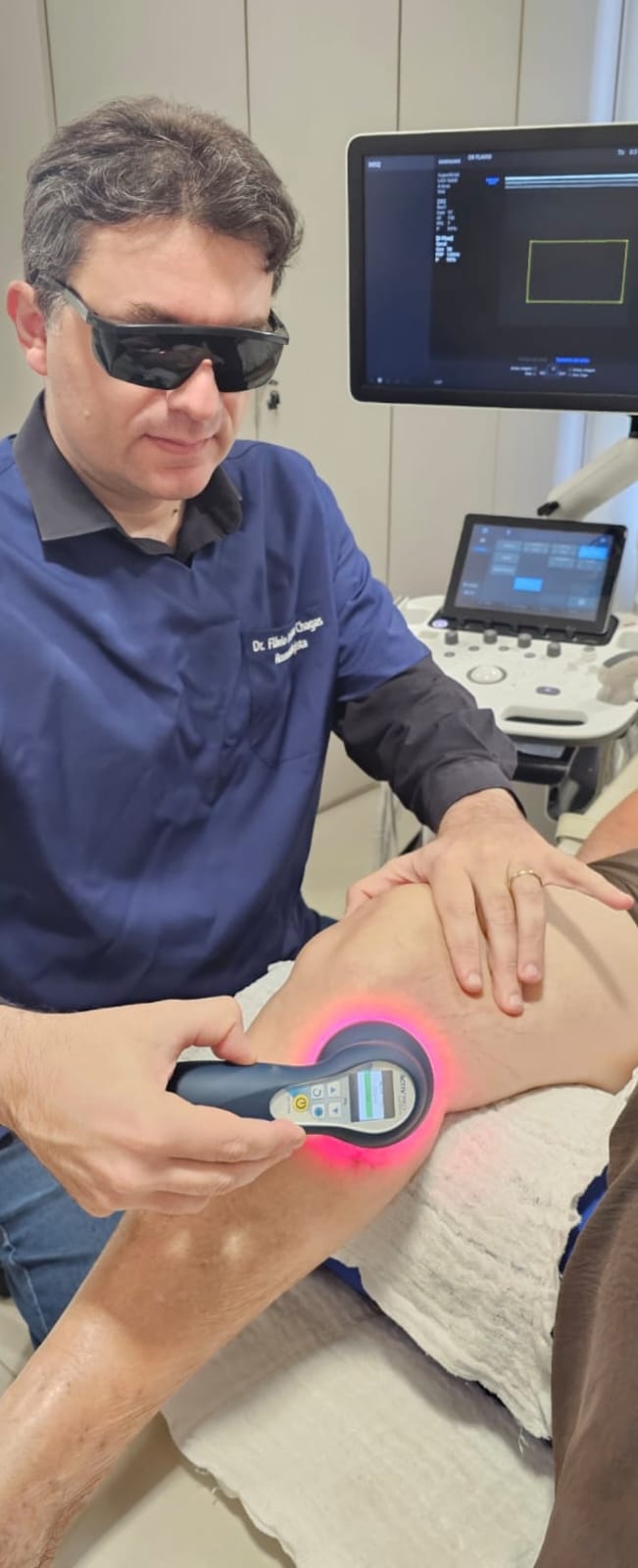 Dr. Flávio aplicando laser terapêutico de fotobiomodulação no joelho de um paciente.